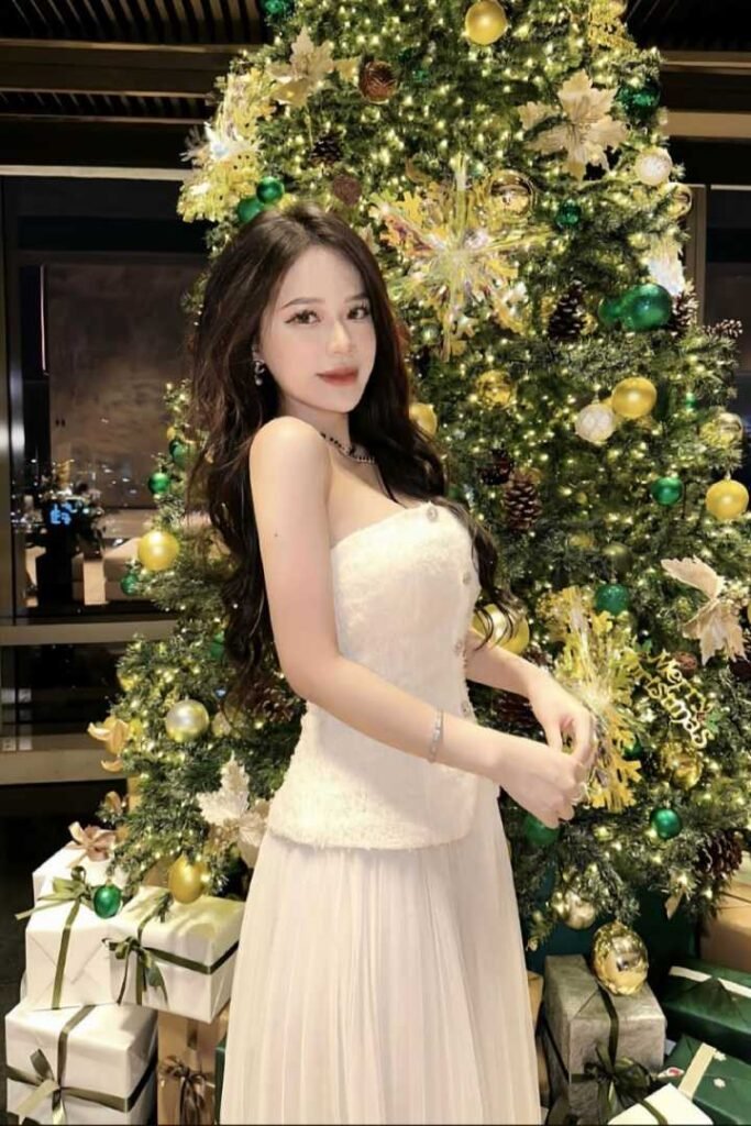 Woman in elegant white dress near a Christmas tree.